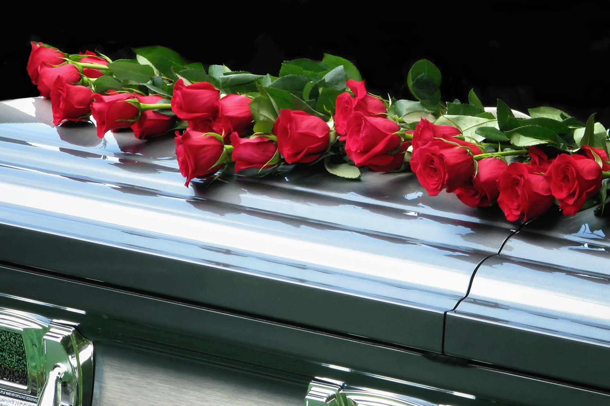Red roses arranged on a polished casket, symbolizing love and remembrance at a funeral. The image conveys emotions of loss and tribute.